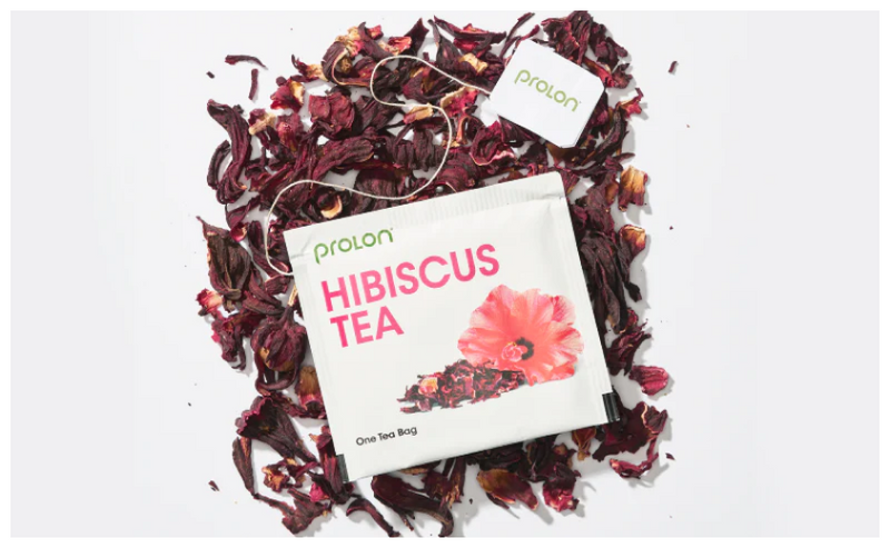 One tea bag of Prolon's Hibiscus Tea on top of dried hibiscus leaves